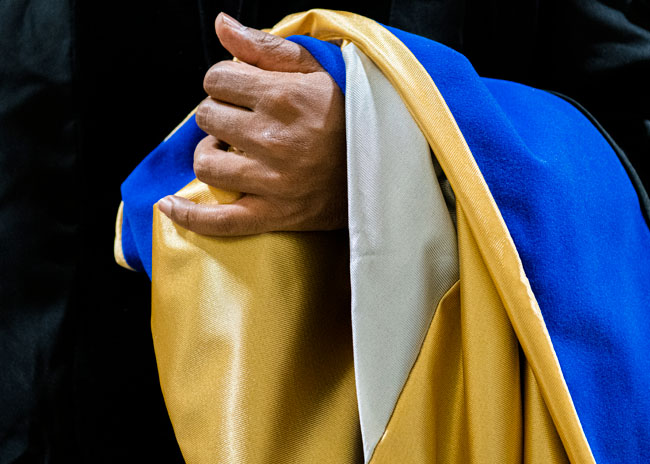 Closeup of a doctoral hood hanging over the forearm and hand.